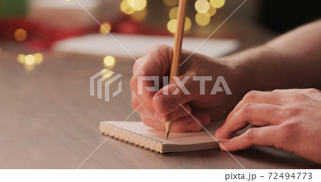 man writes shopping list for holidays in notepad with a pencil under warm light in the evening man writes shopping list for holidays in notepad with a pencil under warm light in the evening 72494773