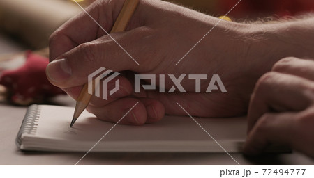 Closeup man writes christmas gifts in notepad with a pencil under warm light in the evening Closeup man writes christmas gifts in notepad with a pencil under warm light in the evening 72494777