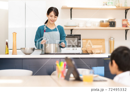 キッチンで料理する母親とテーブルでオンライン授業を受ける男の子 72495332