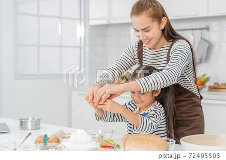 Mother and Daugther is breaking egg to make Bakery in kitchen together, for family love activity concept. 72495505