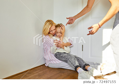a woman sits with a child, calms her down while a man swears at them a woman sits with a child, calms her down while a man swears at them 72497155