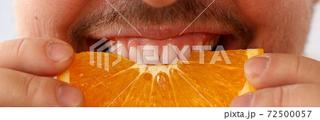 Bearded young man biting juicy orange half Bearded young man biting juicy orange half 72500057