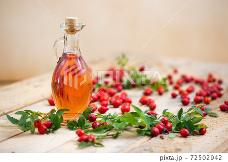 Bottle of rosehip oil laid on wooden table with berries around 72502942