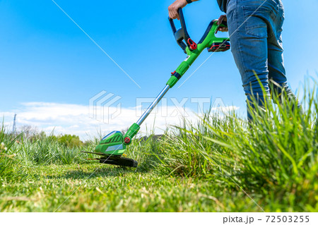 man mows the grass in the meadow with a hand-held cordless lawnmower man mows the grass in the meadow with a hand-held cordless lawnmower 72503255