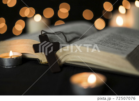 Cross placed on a open bible and candles against bokeh lights background Cross placed on a open bible and candles against bokeh lights background 72507076