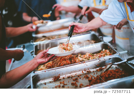 The hand of the wanderer extends to receive food from donations. With volunteers scooping food The hand of the wanderer extends to receive food from donations. With volunteers scooping food 72507711