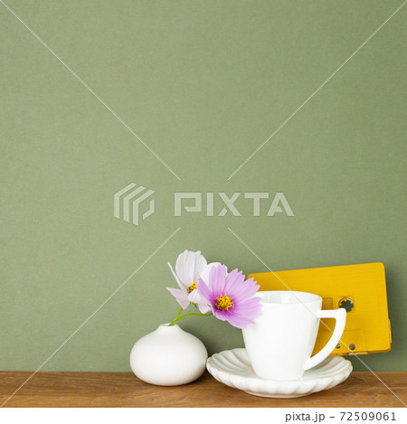 Coffee cup with common cosmos flowers and audio cassette tape on wooden table. Khaki green background Coffee cup with common cosmos flowers and audio cassette tape on wooden table. Khaki green background 72509061