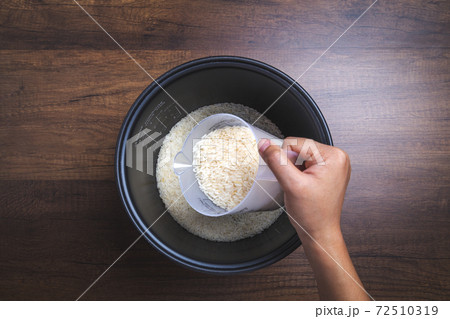 Woman hand is pouring jasmine rice into pot. Using measuring glass. on wooden table. 72510319