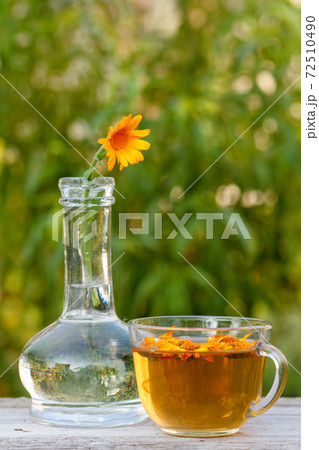 Calendula flower with a stem in a glass flask and cup of tea. 72510490