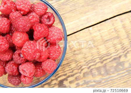 Ripe raspberries in the glass bowl on wooden boards. Ripe raspberries in the glass bowl on wooden boards. 72510669