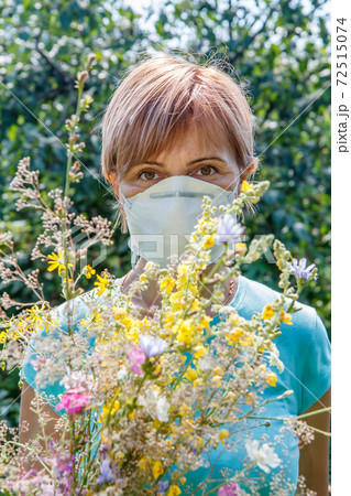 Woman in protective mask holding bouquet of wildflowers. 72515074