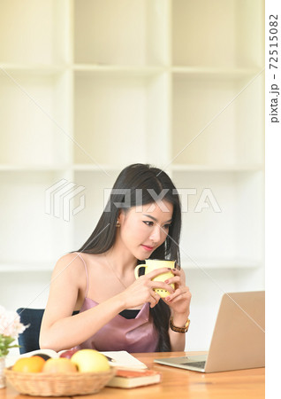 A woman is holding a coffee cup in her hands while sitting in front of a computer laptop. A woman is holding a coffee cup in her hands while sitting in front of a computer laptop. 72515082