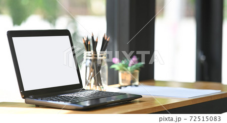 A wooden working desk is surrounding by a white blank screen computer laptop and equipment. A wooden working desk is surrounding by a white blank screen computer laptop and equipment. 72515083