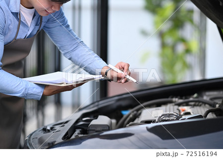 A technician is holding clipboard doing the checklist for repair machine a car in the garage. A technician is holding clipboard doing the checklist for repair machine a car in the garage. 72516194
