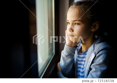 through glass. sad teen girl look out of window outside.  72516538