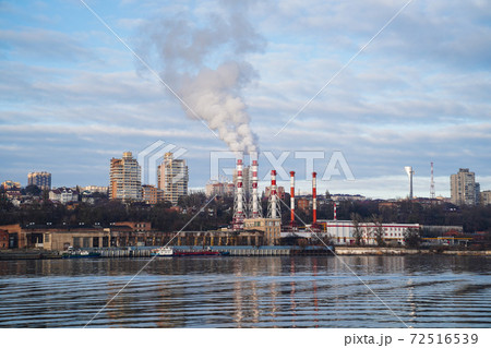 from boiler room tube goes white steam, smoke into sky. Cityscape by river 72516539