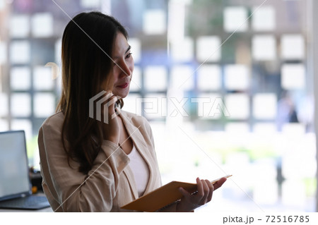 Young businesswoman talking on the mobile phone while holding notebook in modern office. 72516785