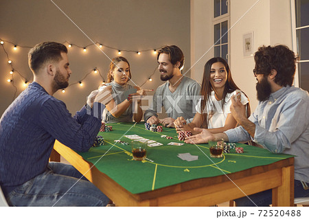 Group of excited friends with playing cards in hands sitting, betting and playing poker Group of excited friends with playing cards in hands sitting, betting and playing poker 72520488