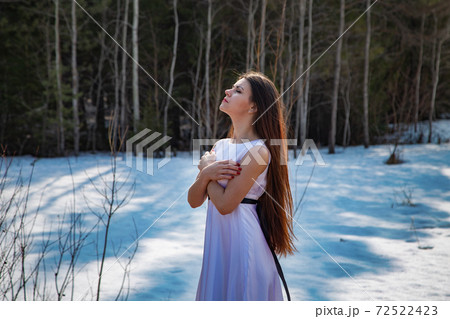 Girl in a white dress with head up and arms crossed among snow 72522423
