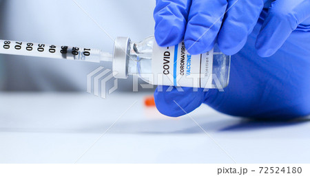 Close-up of infectious doctor or nurse in latex blue rubber gloves holds a syringe and Covid-19 coronavirus vaccine vial 72524180
