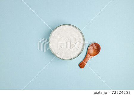 Top view of collagen powder or powder in a glass bowl and small wooden spoon on a blue background with a copy space Top view of collagen powder or powder in a glass bowl and small wooden spoon on a blue background with a copy space 72524252