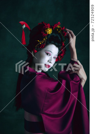 Young japanese woman as geisha on dark green background. Retro style, comparison of eras concept. Young japanese woman as geisha on dark green background. Retro style, comparison of eras concept. 72524909