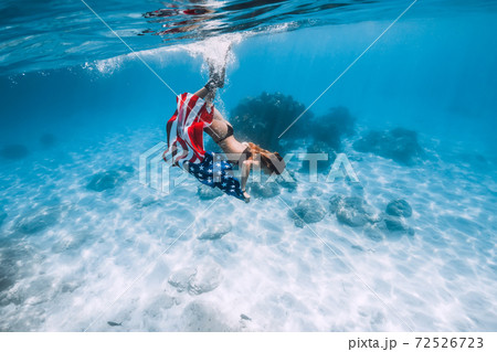 Woman free diver glides underwater over sandy sea with US flag. 72526723