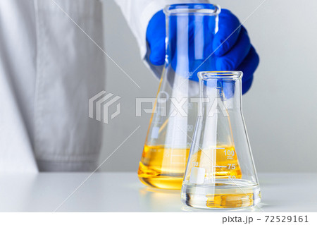 Scientist or doctor in blue gloves pouring some yellow liquid into a flask Scientist or doctor in blue gloves pouring some yellow liquid into a flask 72529161