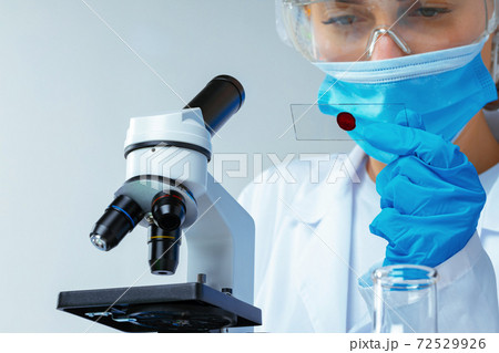 Woman scientist looking at slide with blood sample near microscope in laboratory 72529926