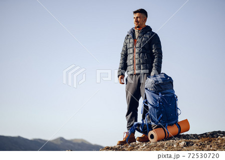 Male backpacker in hiking equipment standing at the top of the mountain 72530720