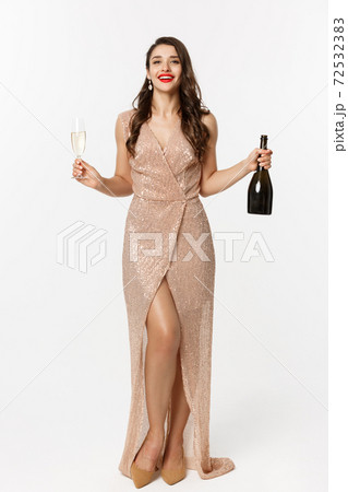Christmas party and celebration concept. Full length of elegant woman with red lips, luxury dress, holding glass of champagne and bottle, white background 72532383