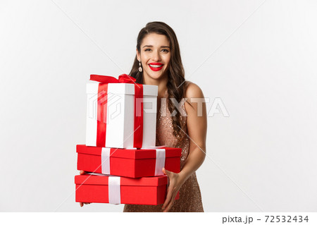 New Year, Christmas and celebration concept. Beautiful woman in party dress, holding gifts and presents, smiling happy, standing over white background 72532434