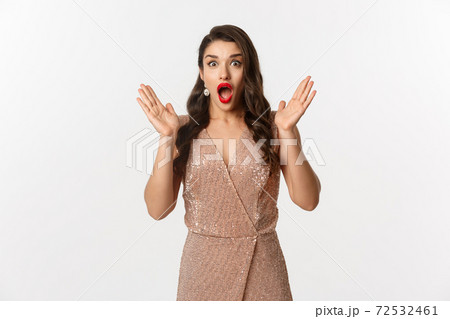 Winter holidays. Beautiful woman in evening dress and makeup, looking surprised and impressed at camera, stare at New Year promo offer, white background Winter holidays. Beautiful woman in evening dress and makeup, looking surprised and impressed at camera, stare at New Year promo offer, white background 72532461
