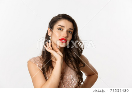 Concept of New Year celebration and winter holidays. Close up of beautiful woman dressed for party, showing luxury earrings and looking sensual at camera, white background 72532480