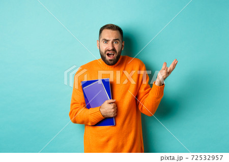 Education. Confused and disappointed man arguing, holding notebooks and complaining, standing over light blue background Education. Confused and disappointed man arguing, holding notebooks and complaining, standing over light blue background 72532957