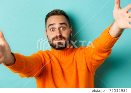 Close-up of handsome happy man reaching hands forward, stretching arms for hug, standing against turquoise background Close-up of handsome happy man reaching hands forward, stretching arms for hug, standing against turquoise background 72532982
