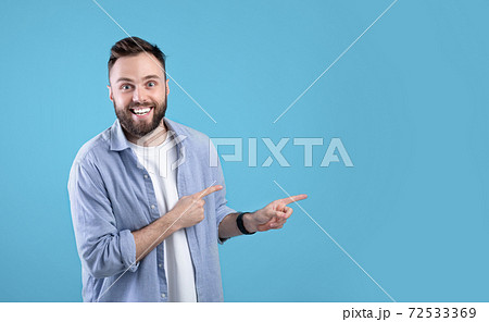 Excited young bearded guy smiling and pointing aside at empty space over blue studio background, panorama Excited young bearded guy smiling and pointing aside at empty space over blue studio background, panorama 72533369