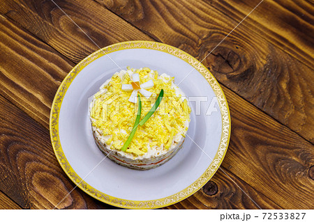 Traditional russian layered salad Mimosa with spring decoration Daffodil. Decoration is made of egg, green onion and carrot. Top view Traditional russian layered salad Mimosa with spring decoration Daffodil. Decoration is made of egg, green onion and carrot. Top view 72533827