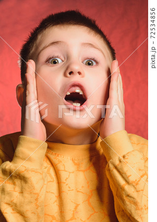 The boy smiles in surprise and gestures with his hands, pressing them to his face. The boy smiles in surprise and gestures with his hands, pressing them to his face. 72534856