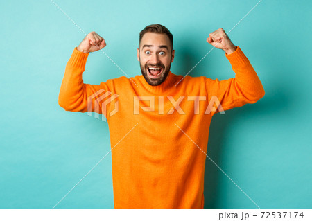 Handsome man celebrating victory, winning and looking happy, triumphing over win, standing over light blue background 72537174