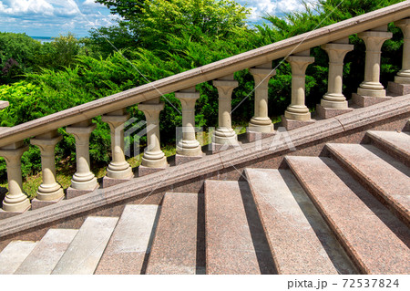 granite stone stairs details of steps and railings with balustrades in the background landscape with thuja bushes and cloudy sky on a sunny summer day. 72537824