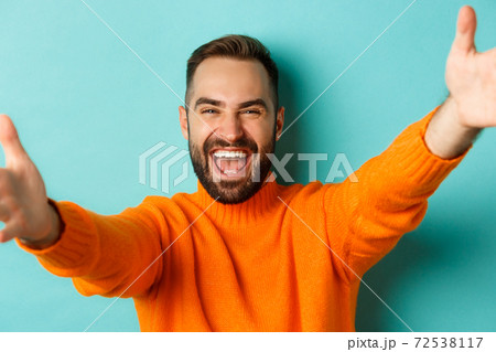 Close-up of handsome happy man reaching hands forward, stretching arms for hug, standing against turquoise background Close-up of handsome happy man reaching hands forward, stretching arms for hug, standing against turquoise background 72538117