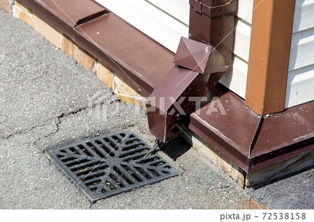 stormwater pipe on the wall of the building facade with rainwater drainage into the drainage system with a sewer manhole grill. 72538158
