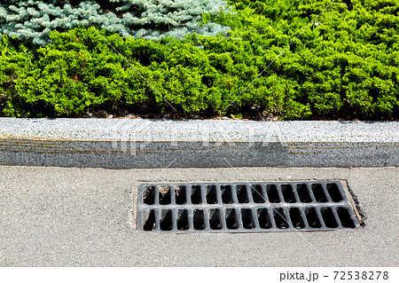 drainage system of an asphalt road with a manhole grill for sewage near the border with green plantings. 72538278