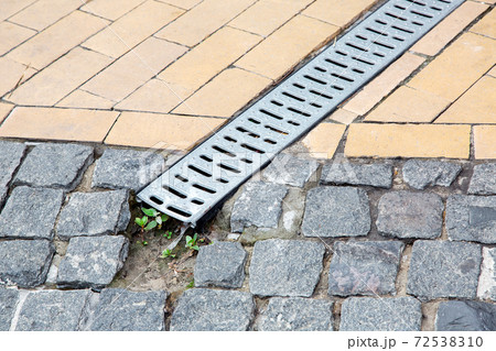 A stainless steel lattice of a drainage paving system on a walkway made of square stone tiles, close up of a rainwater drainage system, nobody. 72538310