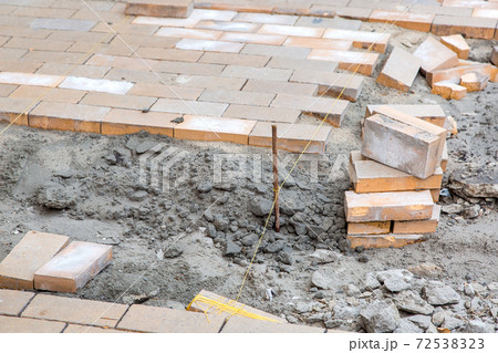 paving of a new sidewalk from rectangular stone tiles according to the marks of the stretched thread of the level, a close-up of the repair work of the stone path. 72538323