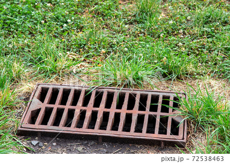 storm hatch sewage with a rusty grill overgrown with weeds in the park, close up of drainage system. storm hatch sewage with a rusty grill overgrown with weeds in the park, close up of drainage system. 72538463