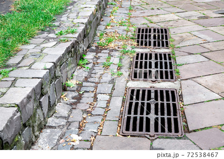 the iron grate of the drainage system hatch on the footpath paved with paving stones, closeup. the iron grate of the drainage system hatch on the footpath paved with paving stones, closeup. 72538467