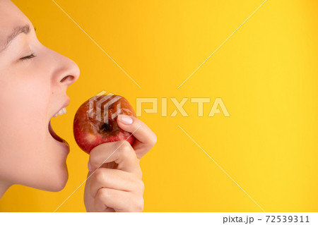 The girl bites a rotten apple with a worm on a yellow background. Expired products, junk food The girl bites a rotten apple with a worm on a yellow background. Expired products, junk food 72539311