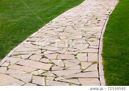 flagstone footpath in a park with a green lawn goes into perspective on a sunny summer day, close-up of paving stone tiles. flagstone footpath in a park with a green lawn goes into perspective on a sunny summer day, close-up of paving stone tiles. 72539592
